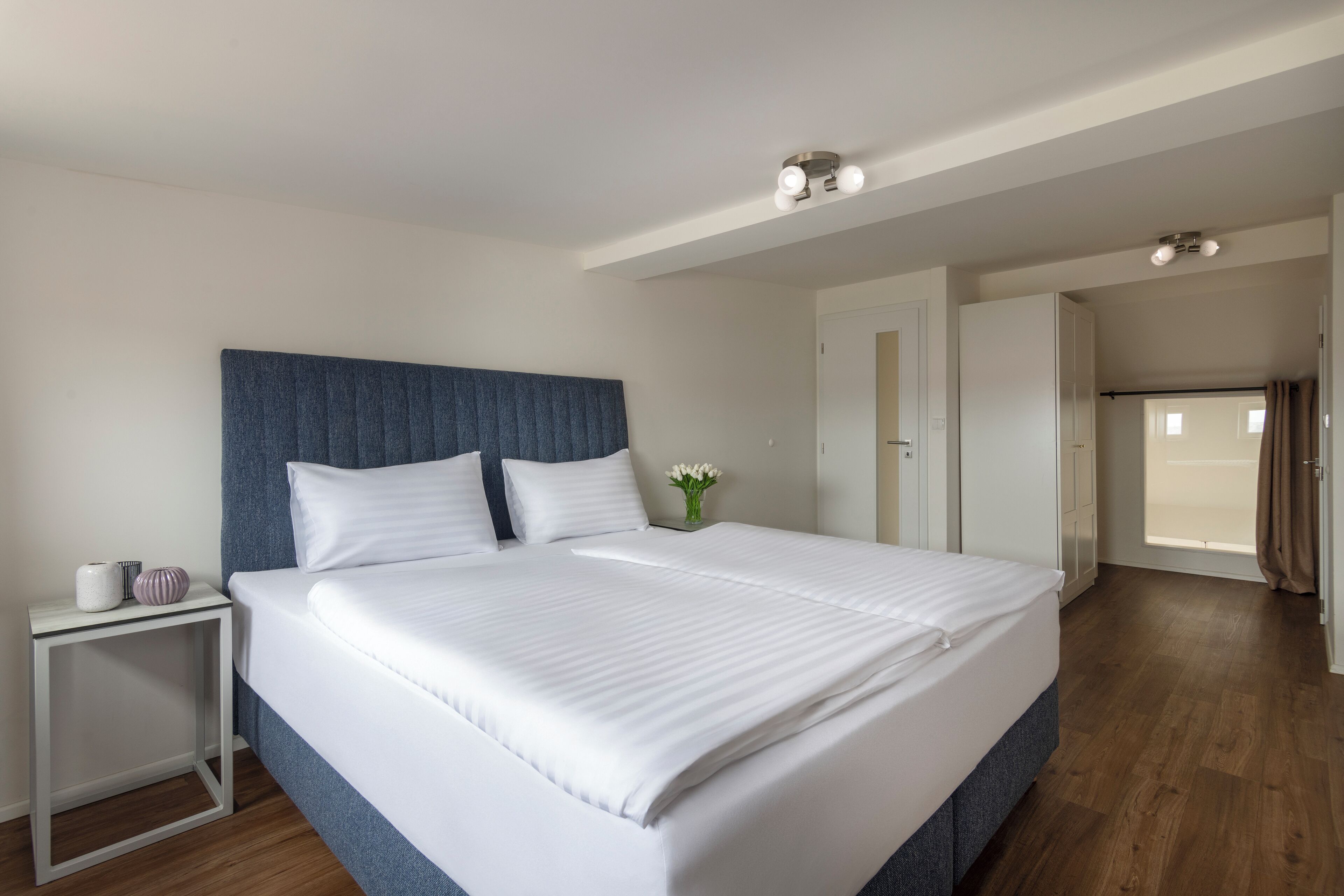 A spacious bedroom with a large bed, a bedside table, and a view of the outside.