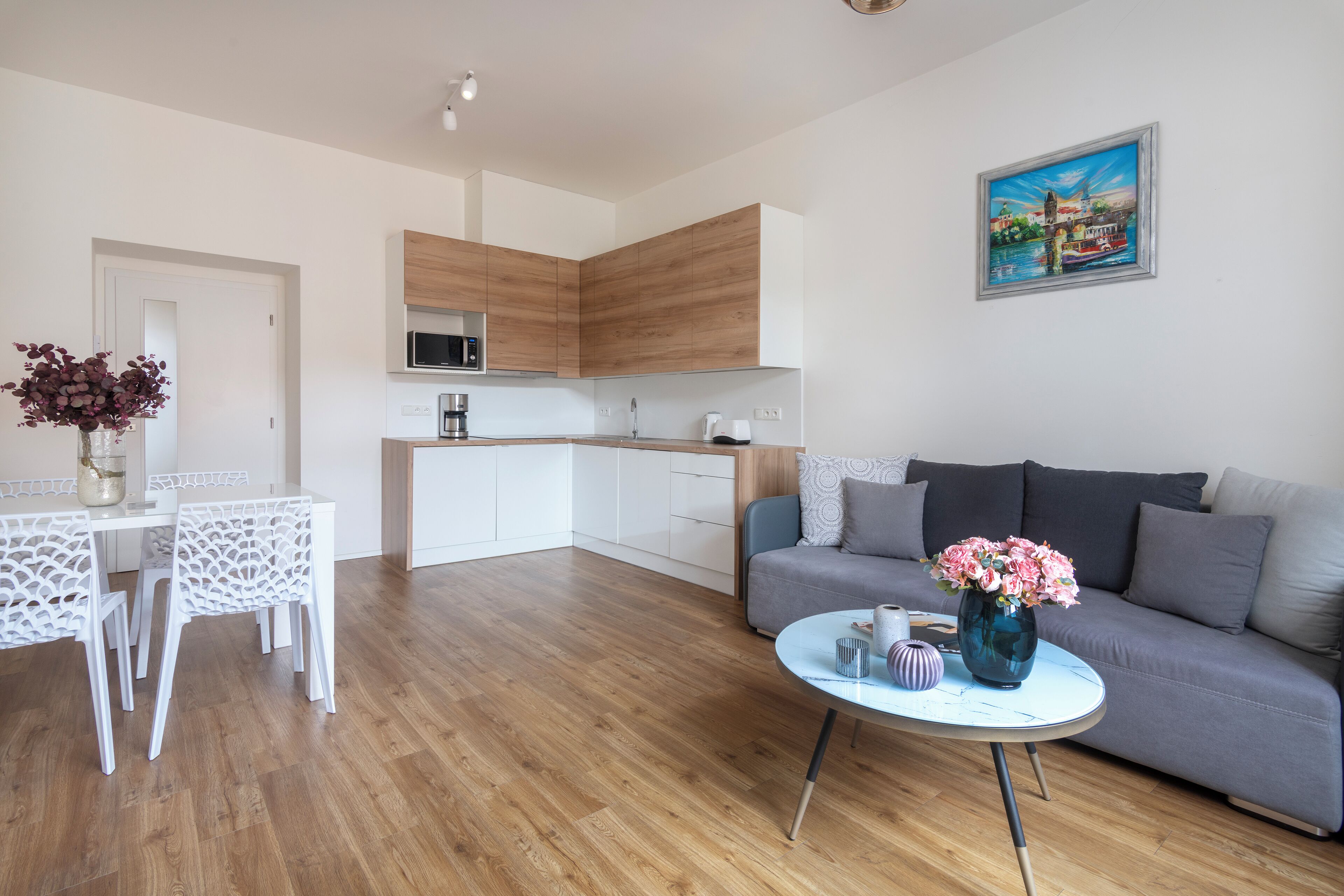 A modern living room with a grey sofa, a round coffee table, and a dining area with white chairs.