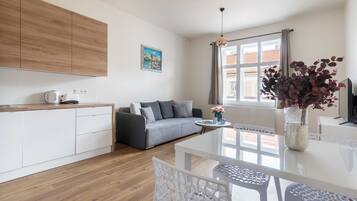 Eine moderne Küche mit weißen Schränken, einem grauen Sofa und einem Esstisch mit weißen Stühlen.