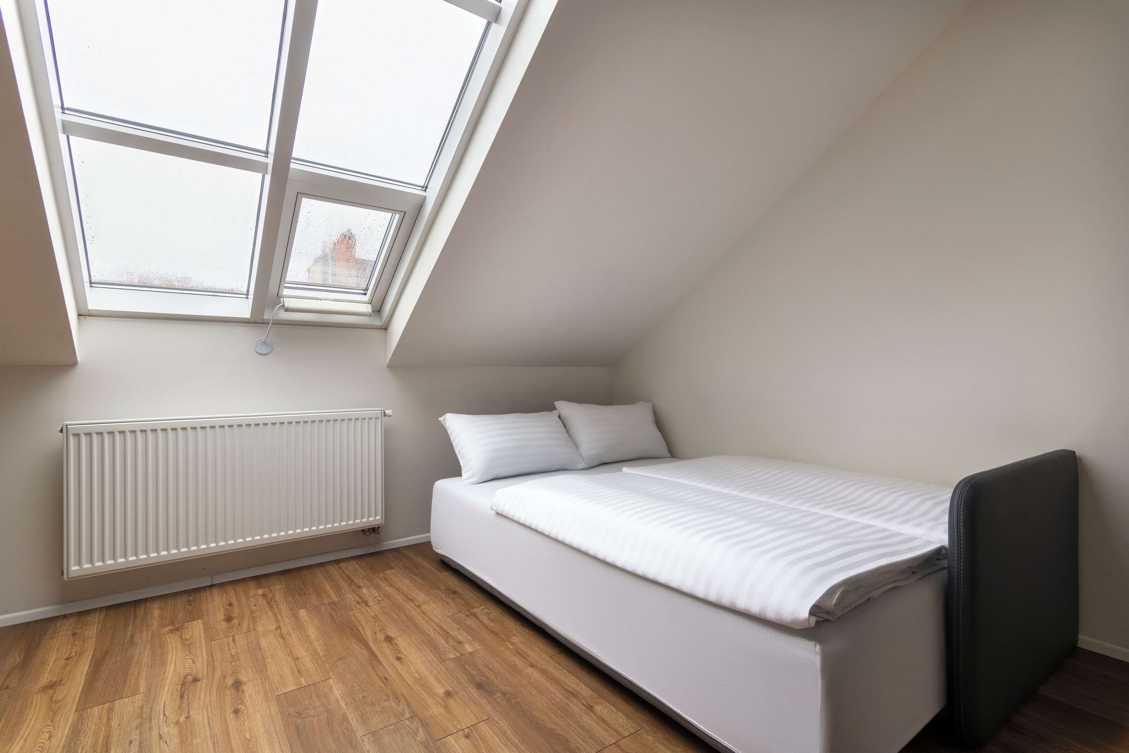 A small, single-bed room with a sloped ceiling and a skylight.