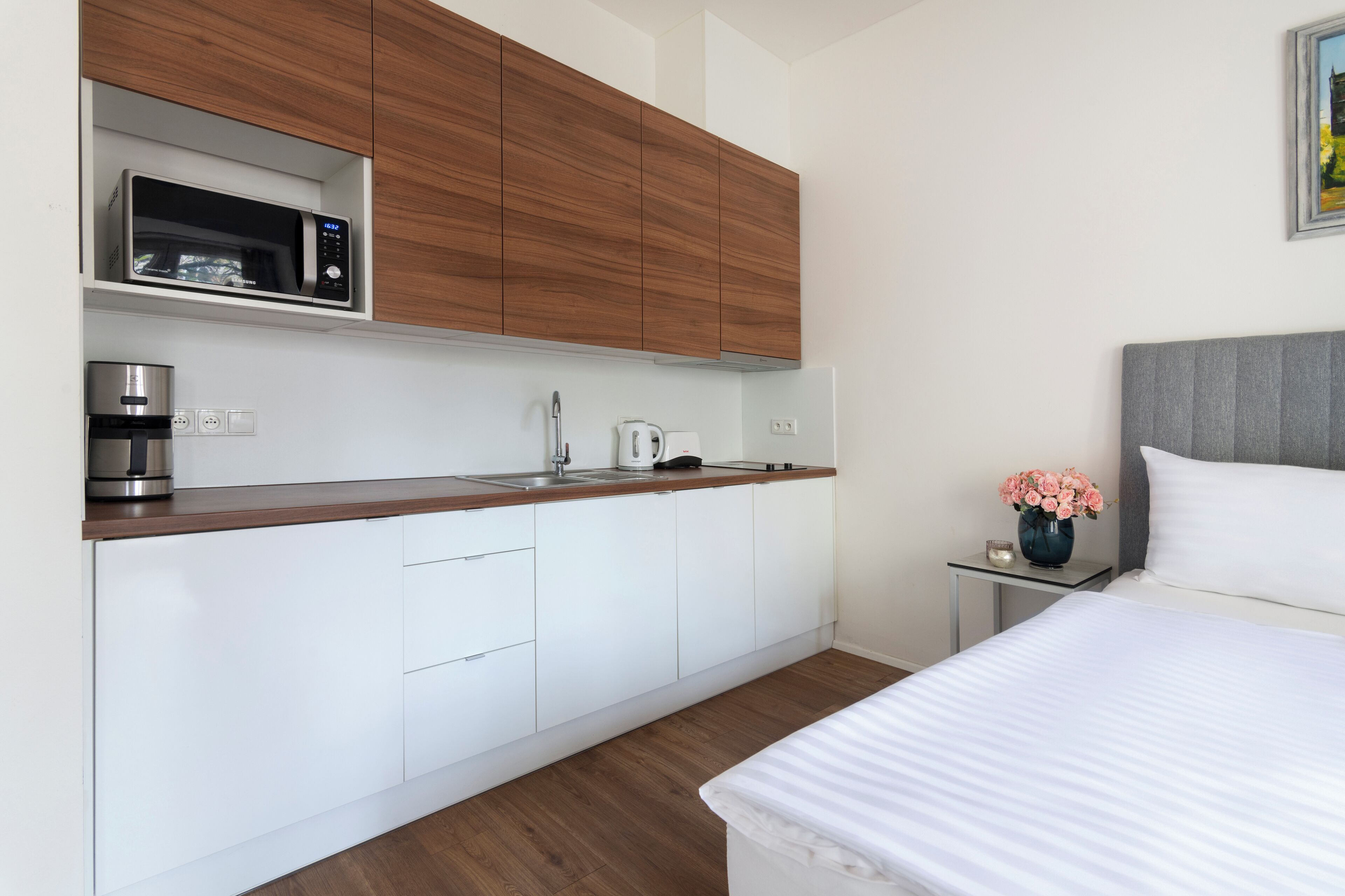 A modern kitchen with white cabinets, a microwave, and a coffee maker. There is a small side table with a vase of flowers.