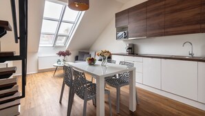 Eine moderne Küche mit weißer Arbeitsplatte, einer eingebauten Mikrowelle und einer Kaffeemaschine. Es gibt einen Esstisch mit Stühlen und eine Blumenvase.