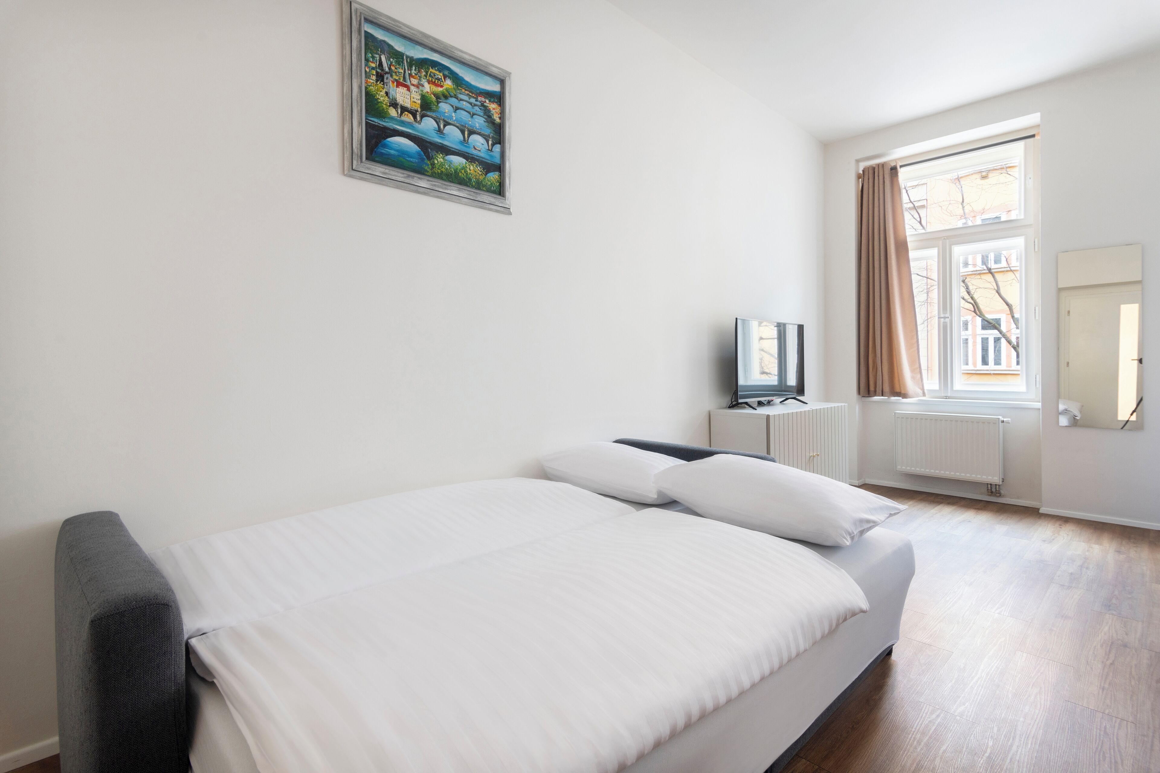 A bedroom with a bed, a TV, a radiator, and a window with curtains.