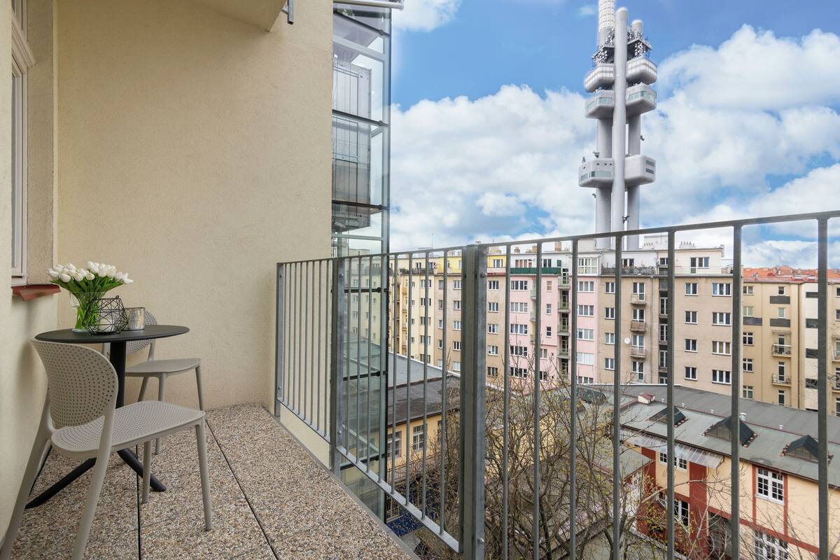 Un balcon avec une table et des chaises, donnant sur un paysage urbain avec des immeubles et une tour.
