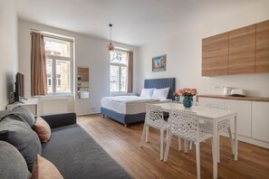 Een moderne kamer met een bed, een slaapbank, een eettafel met stoelen, een keukenhoek en een groot raam.