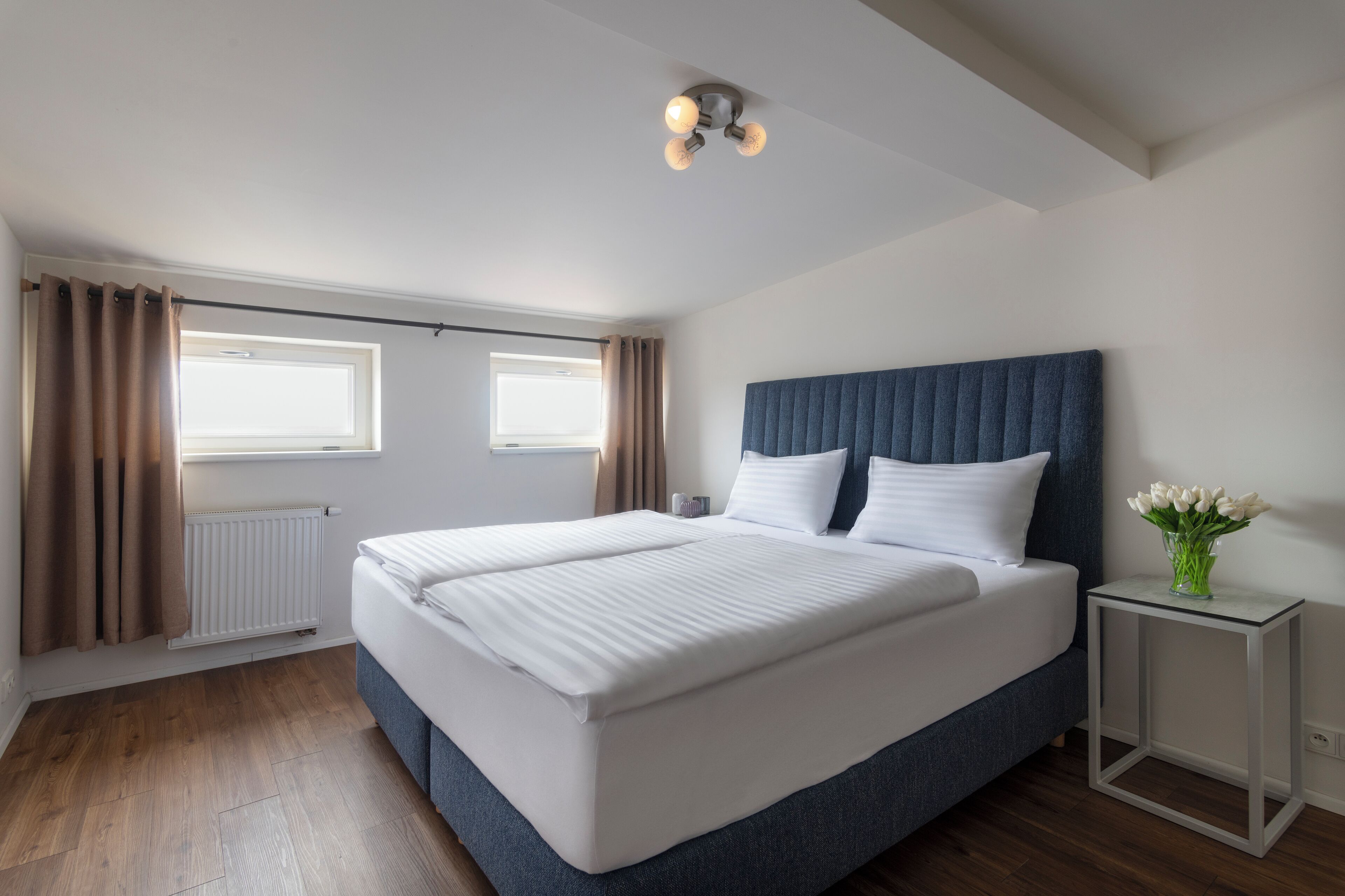 Un dormitorio moderno con una cama grande, una mesita de noche con un florero y una lámpara en el techo.