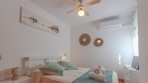 A bedroom with a bed, bedside tables, a ceiling fan, wall art, and an air conditioning unit. - 090 - Altomar II 005 - comfortHOLIDAYS (el Gran Alacant)
