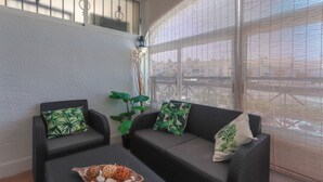 A sunlit room with a sofa and two chairs, a small table with decorative items, and a large window with blinds. - 090 - Altomar II 005 - comfortHOLIDAYS (el Gran Alacant)