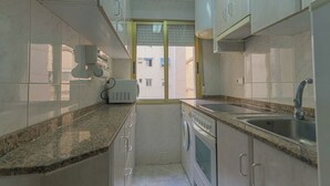 Una cocina compacta con encimeras de granito, electrodomésticos de acero inoxidable y armarios blancos.