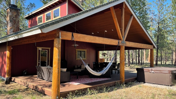A cabin with a covered porch, a hammock, outdoor seating, and a hot tub.