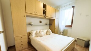 A bedroom with a bed, wooden wardrobe, and a shelf unit. - GIULY BETH'S HOUSE BRENZONE (Assenza)