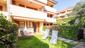 A two-story building with a balcony, a grassy yard, and a seating area with chairs. - GIULY BETH'S HOUSE BRENZONE (Assenza)