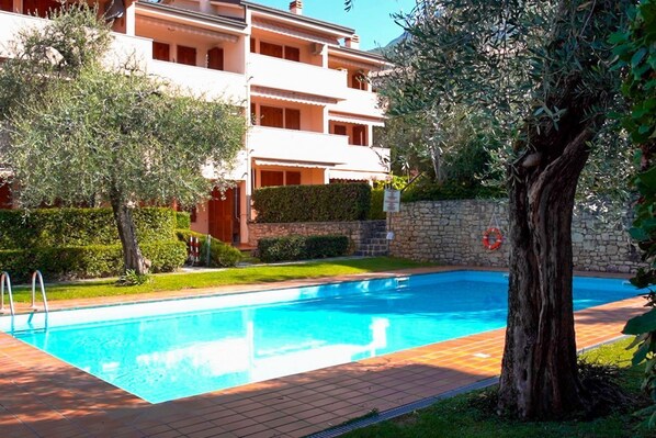 A swimming pool with a tiled deck, surrounded by a stone wall and greenery.