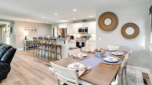 A modern kitchen with white cabinets, stainless steel appliances, and a dining area with a wooden table set for four. - Beautiful Kentucky Lake Getaway w/ Dock & Deck! (New Concord)