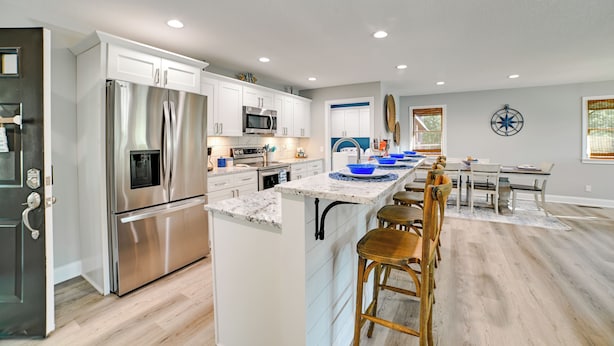 A modern kitchen with stainless steel appliances, a central island with bar stools, and a dining area with a table and chairs. - Beautiful Kentucky Lake Getaway w/ Dock & Deck! (New Concord)