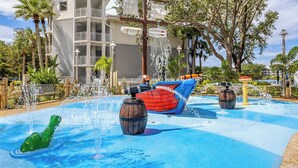 A water park area with a pool, a boat-shaped water slide, and a large tree.