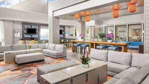 A modern living room with a sectional sofa, a dining area with bar stools, and a kitchen with a TV.