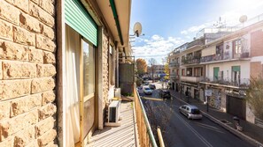 A balcony with a view of a street, a brick building, and a satellite dish.