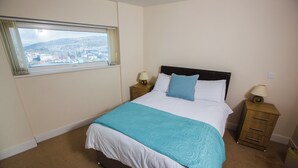 Un dormitorio con cama, dos mesitas de noche, una ventana con vistas y suelo alfombrado.