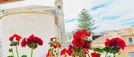 Un balcón con flores rojas y vistas a un edificio con una torre.