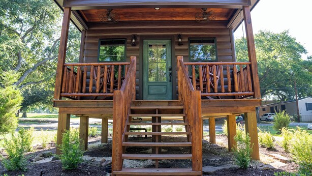 A wooden cabin with a front porch, a green door, and a staircase leading up to it. - Deluxe Rustic Tiny Cabin (Broussard)