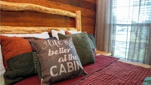 A bed with a wooden headboard, multiple pillows, and a red blanket. - Deluxe Rustic Tiny Cabin (Broussard)