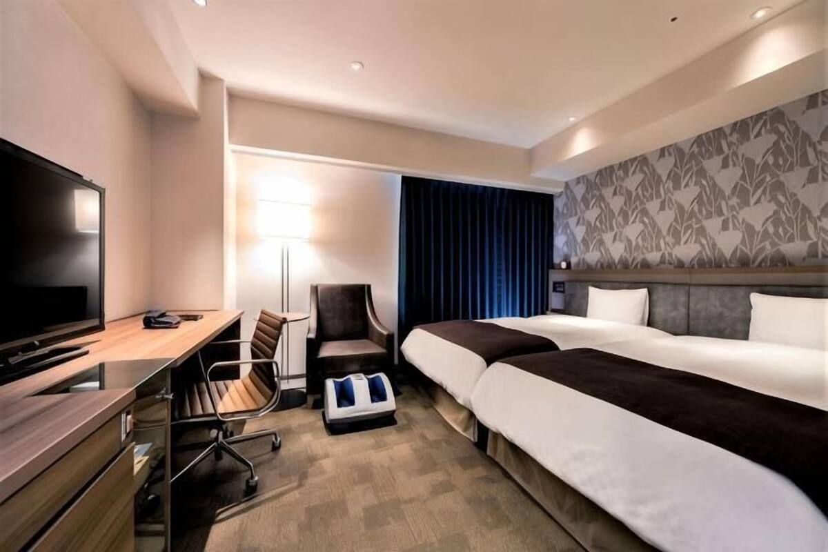 A hotel room with a bed, a desk with a computer, a TV, and a chair.