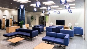 Un vestíbulo moderno con sofás azules, mesas de madera y lámparas colgantes.