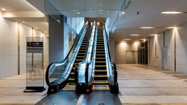 Un área de ascensores moderna con tres escaleras mecánicas, un panel de control y un techo de cristal.