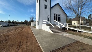 A two-story white building with a central staircase and a small porch area. - Sanctuary Parish 18Ft ceilings, 5 bedrooms, & 3 baths (Danbury)
