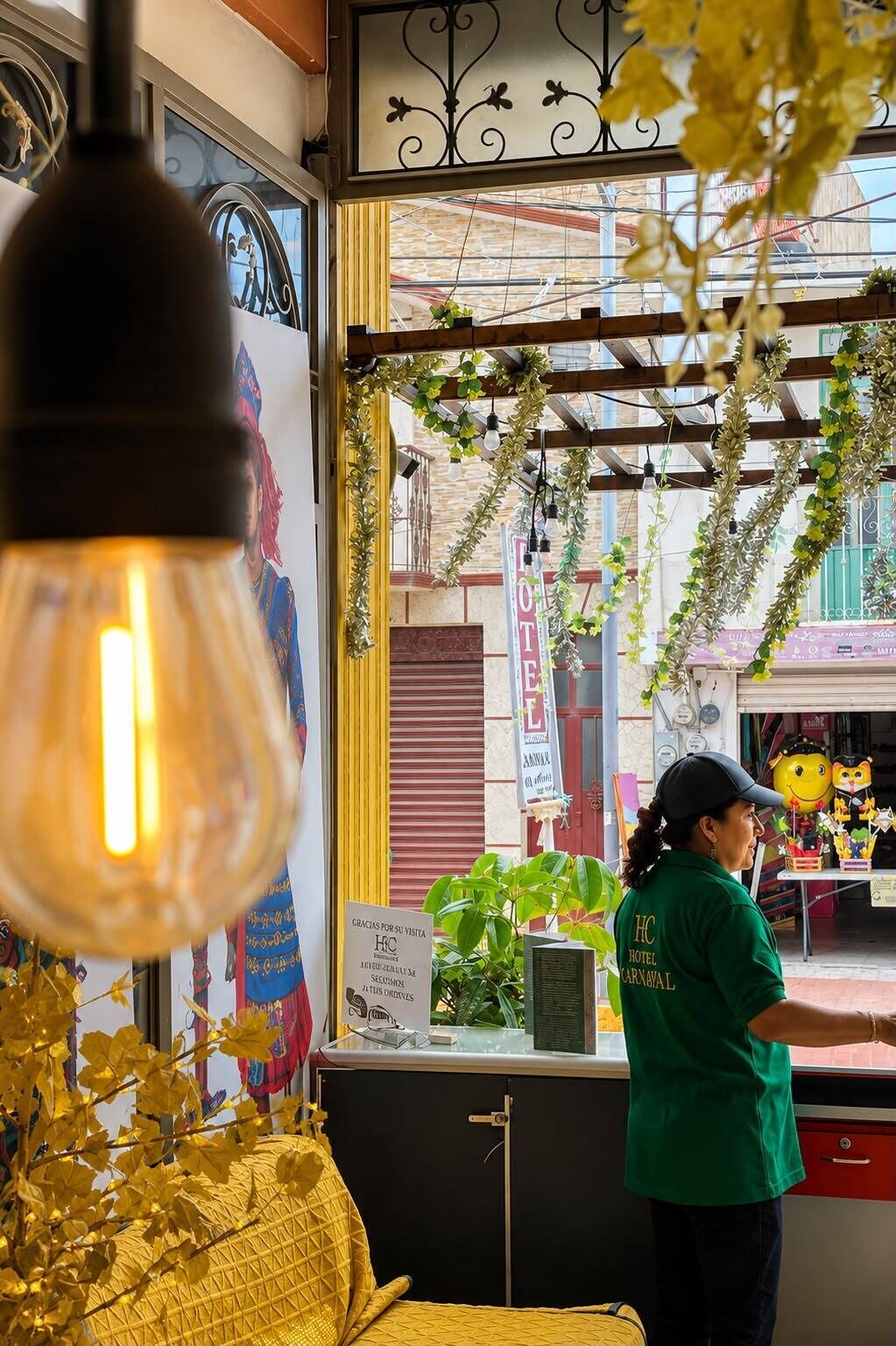 A hotel interior with a view of the street, a staff member in uniform, and a sign indicating the hotel name.