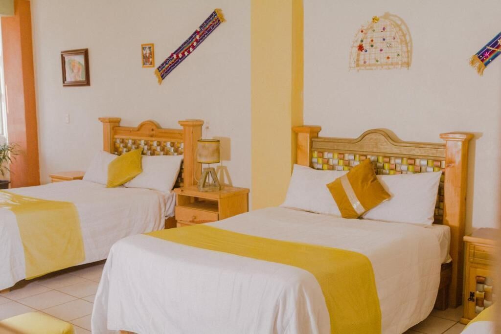 Ein Hotelzimmer mit zwei Betten, jeweils mit einem hölzernen Kopfteil und weißer Bettwäsche. An den Betten befinden sich Nachttische mit Lampen und eine kleine Ablagefläche.