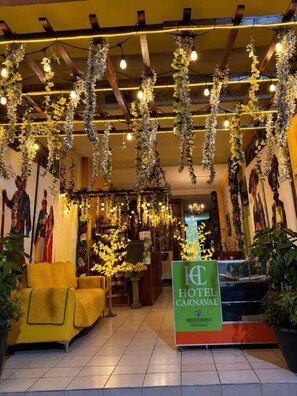 A hotel lobby with hanging floral arrangements, a reception desk, and a seating area. - Hotel Carnaval  (Huejotzingo)