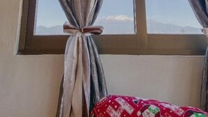 Una habitación con ventana cubierta por cortinas, una cama con manta roja y un adorno colgado en la pared.