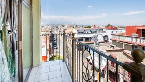 Un balcón con vista a un paisaje urbano, con edificios de techos rojos y cielo despejado.
