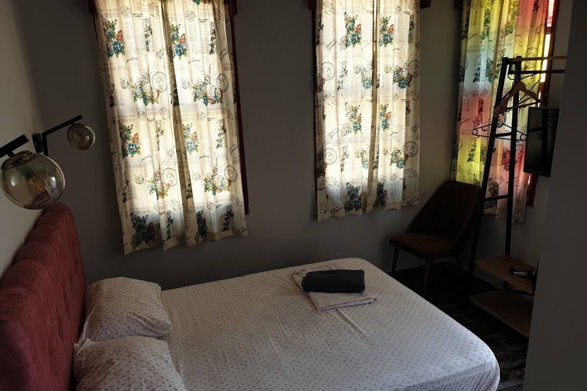 Ein Schlafzimmer mit einem Bett, zwei Vorhängen, einem Sessel und einem kleinen Tisch.