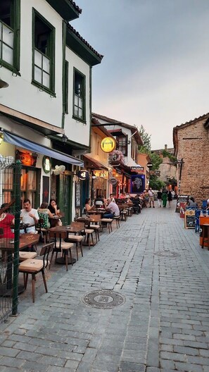 A cobblestone street lined with traditional buildings, outdoor seating at cafes, and pedestrians. - Callisto Pub & Kitchen & Hotel (Antalya)