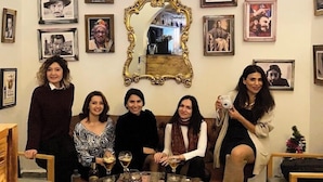 Un grupo de personas sentadas alrededor de una mesa redonda con bebidas, rodeadas de cuadros en las paredes.