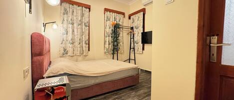 A small room with a bed, a red chair, a television, and a window with curtains.