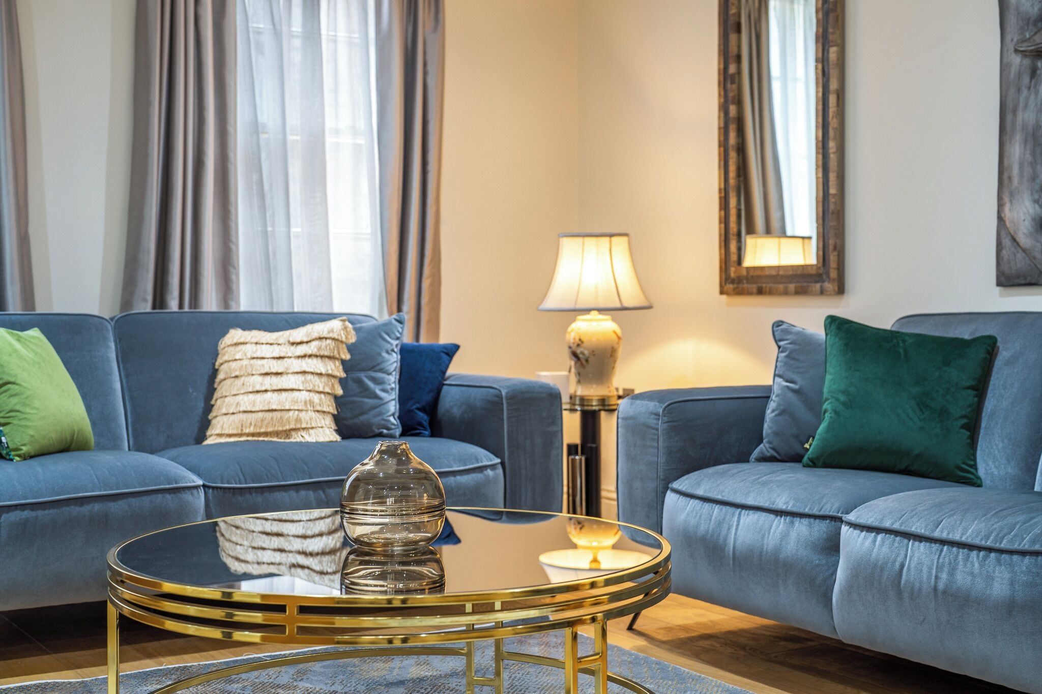 Ein Wohnzimmer mit zwei blauen Sofas, einem runden Glastisch und einer Lampe.