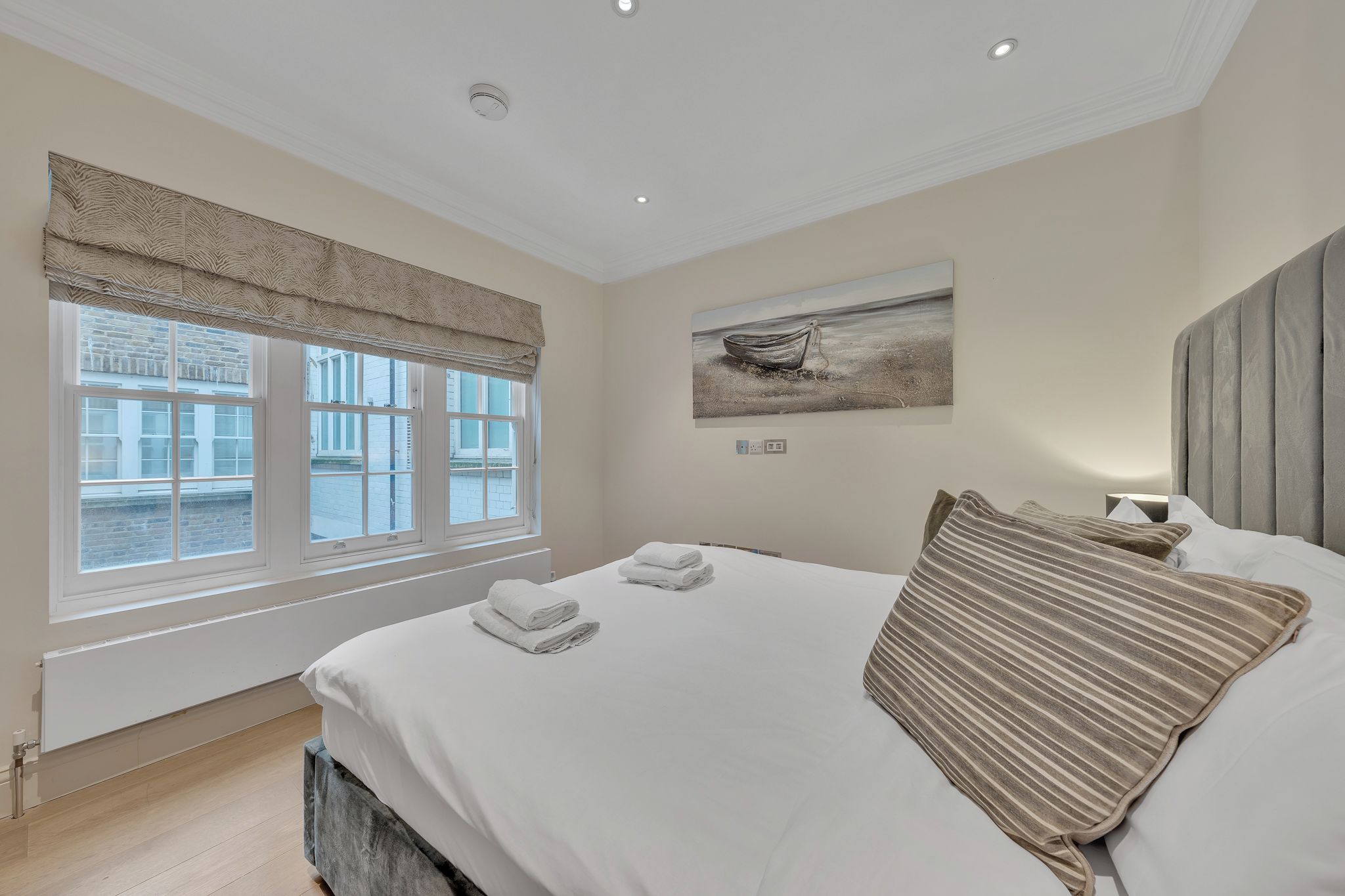 A hotel room with a large bed, a window with blinds, a painting on the wall, and a radiator.