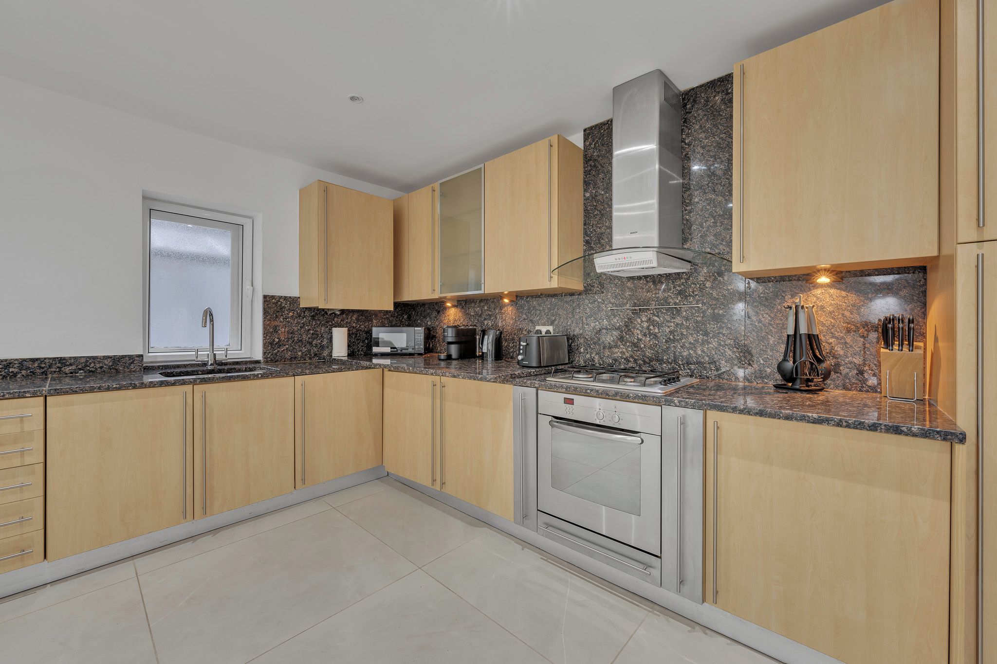 A modern kitchen with wooden cabinets, a stainless steel range hood, a built-in oven, and a granite countertop.