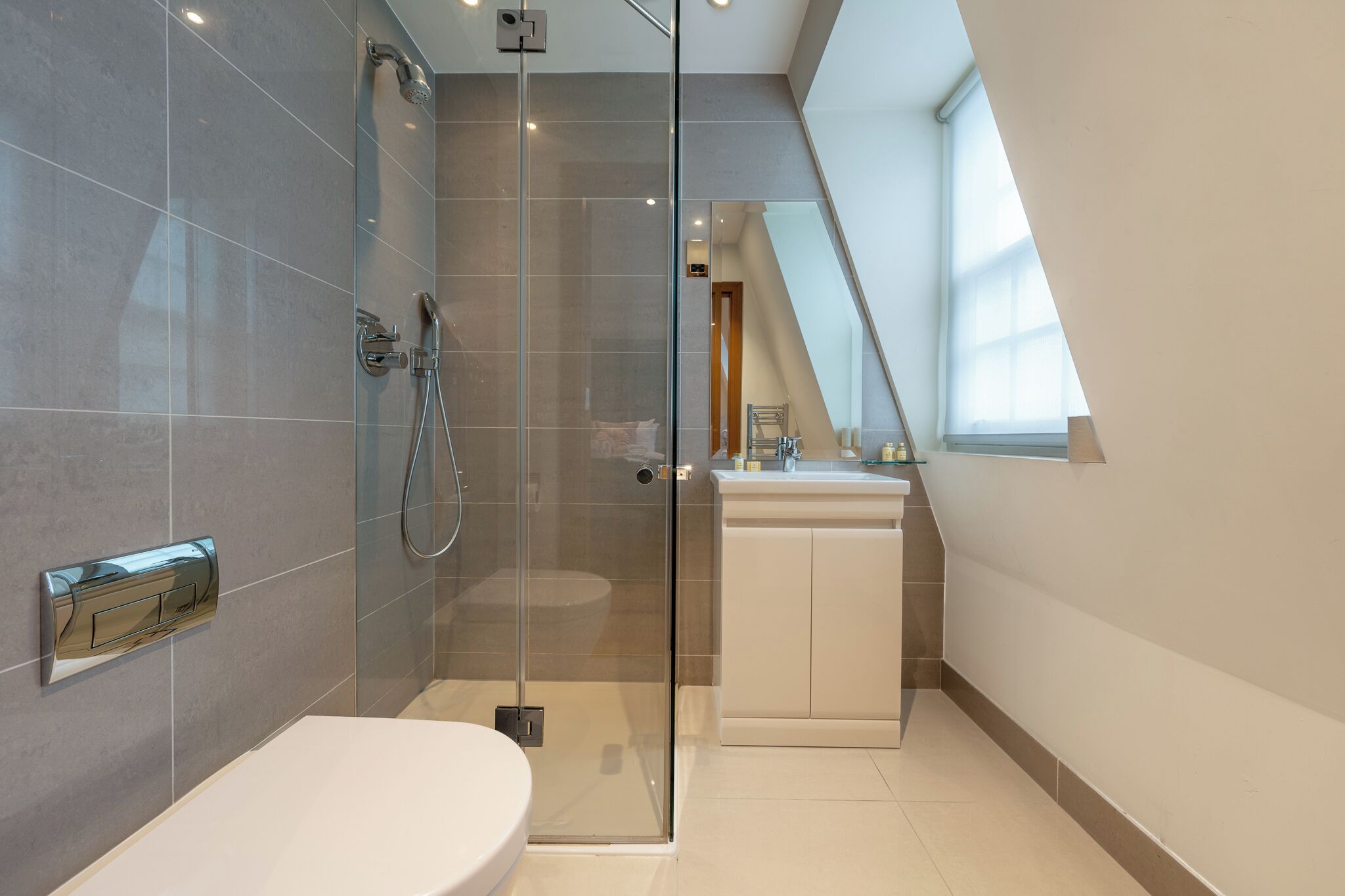 Un baño moderno con ducha de vidrio, lavamanos blanco y un amplio ventanal que proporciona luz natural.