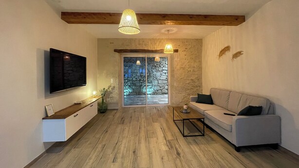 A modern living room with a flat-screen TV, a sofa, a coffee table, and a stone wall. - Logement Une Petite Escale Lectoure (Lectoure)