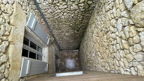 A stone-walled room with a wooden floor, a window with blinds, and a door. - Logement Une Petite Escale Lectoure (Lectoure)