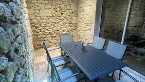 A stone-walled patio with a wooden ceiling and a table with chairs. - Logement Une Petite Escale Lectoure (Lectoure)