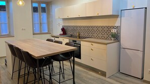 A modern kitchen with a wooden dining table, black bar stools, a built-in oven, and a white refrigerator. - Logement Une Petite Escale Lectoure (Lectoure)