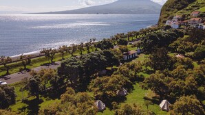 A coastal landscape with a prominent mountain, a beach, and a residential area with houses and trees. - Bearsu Nature Almoxarife (Horta)