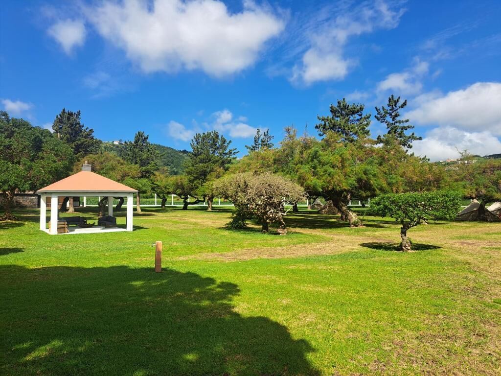 A gazebo in a park with trees and a clear sky.