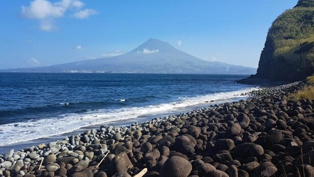 A rocky beach with a mountain in the background. - Bearsu Nature Almoxarife (Horta)